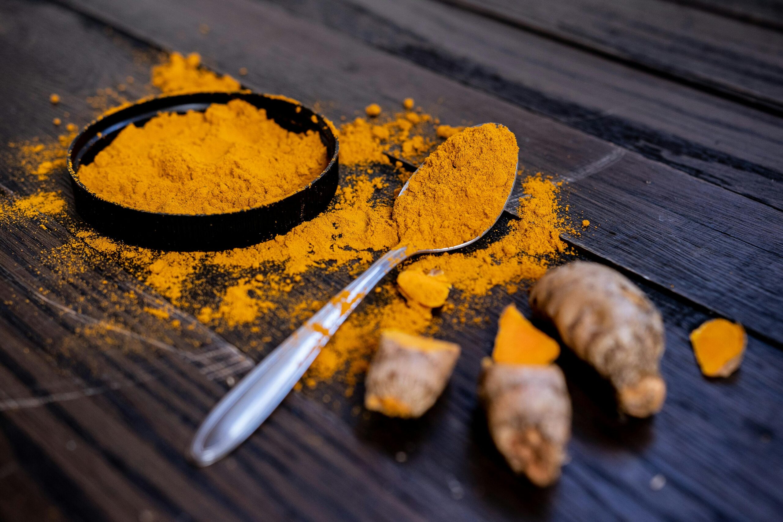 Fresh turmeric root and ground turmeric powder in a dark bowl with spoon on dark wood surface