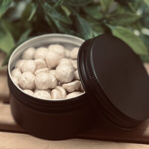 Angled view of open black matte tin filled with natural mica dusted solid lotion pearls handcrafted in small batches in North Carolina