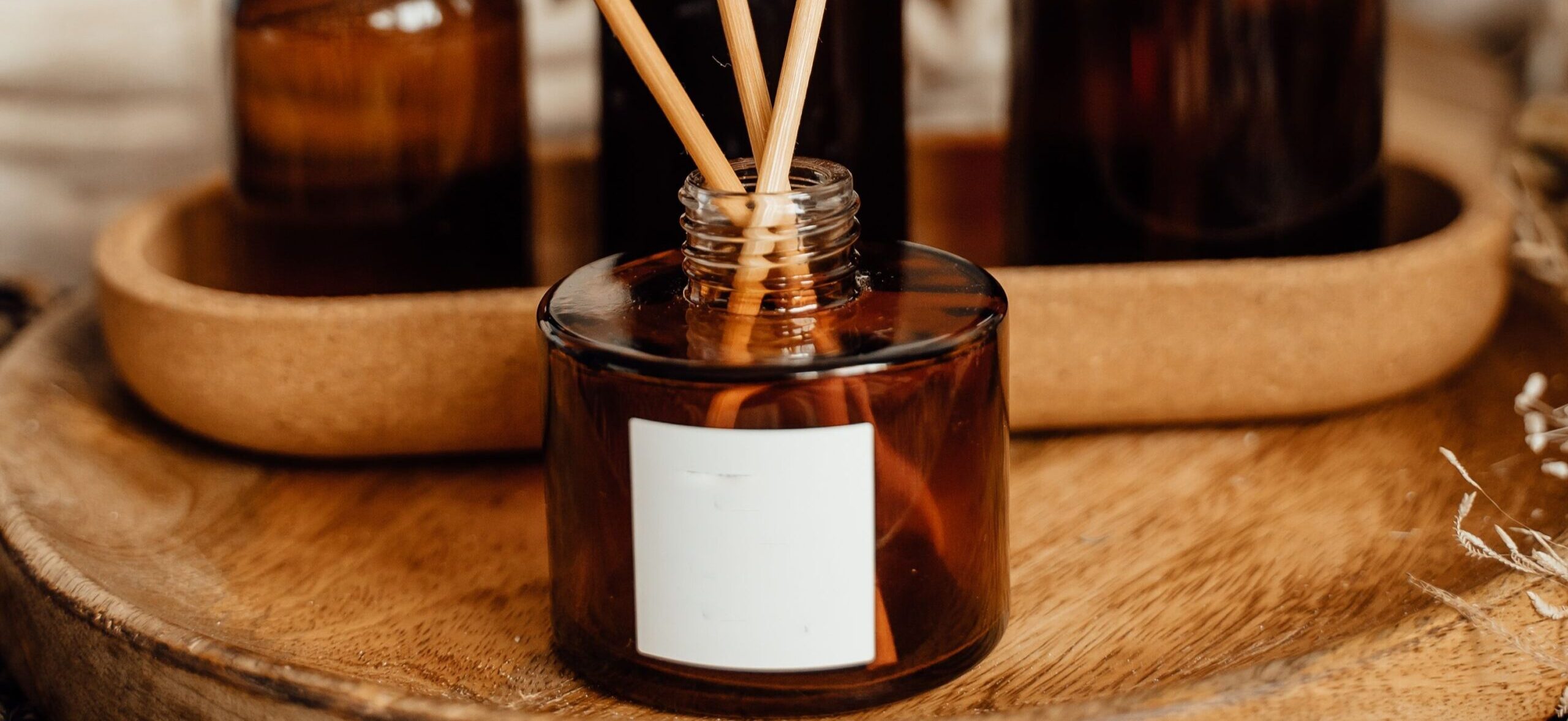 A reed diffuser with bamboo reeds on a wooden tray beside amber glass bottles in a home setting